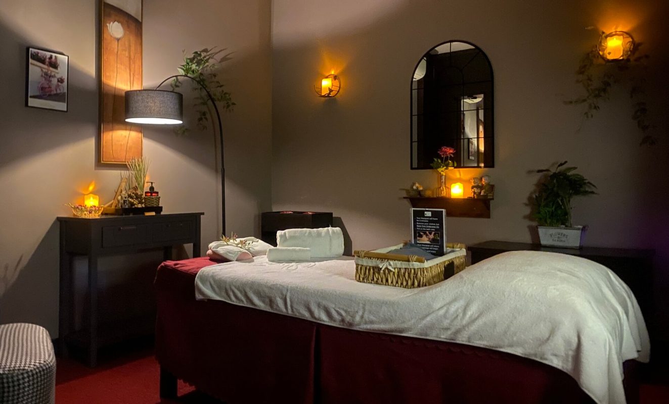 Spa services room prepared for treatments with one massage bed and soft lighting with candlelight accents.